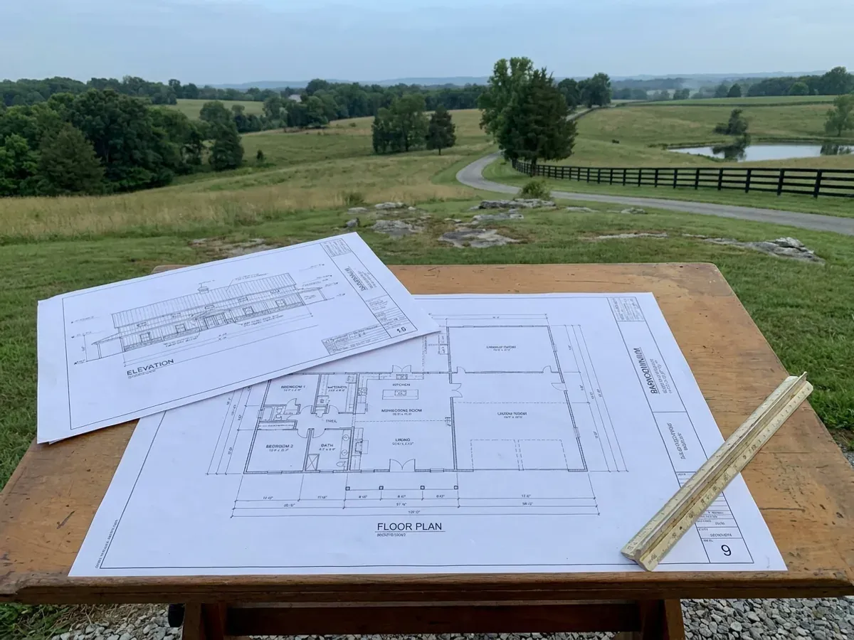 Barndominium floor plan and elevation drawings laid out on a drafting table with a scale rule.