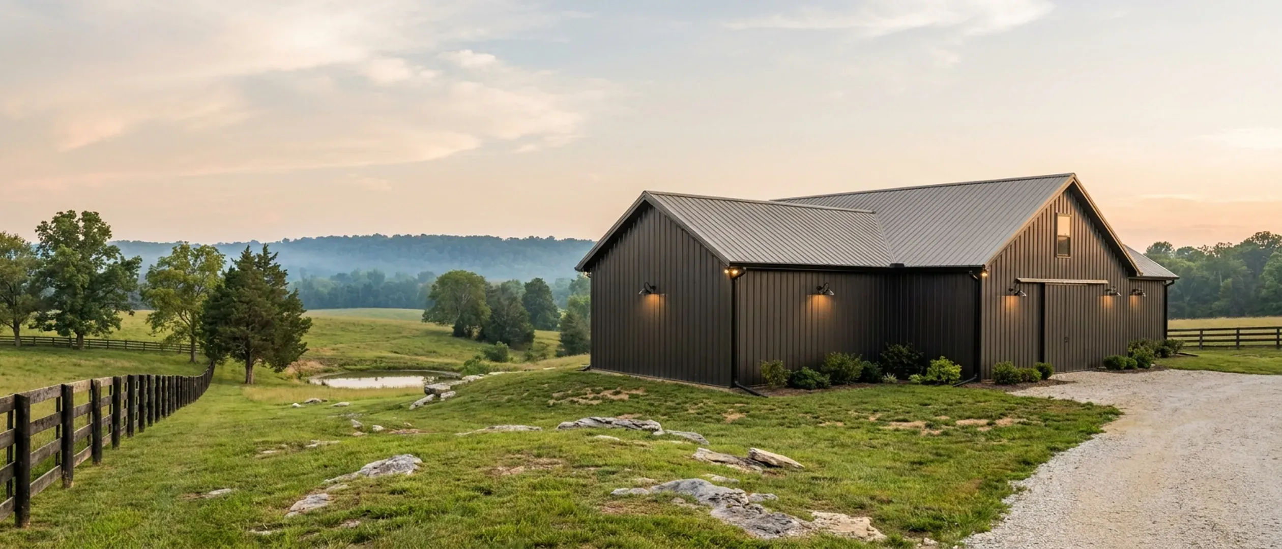 A completed barndominium viewed from a low angle showing its standing seam metal roof, vertical wall panels, gutters and exterior wall lights.