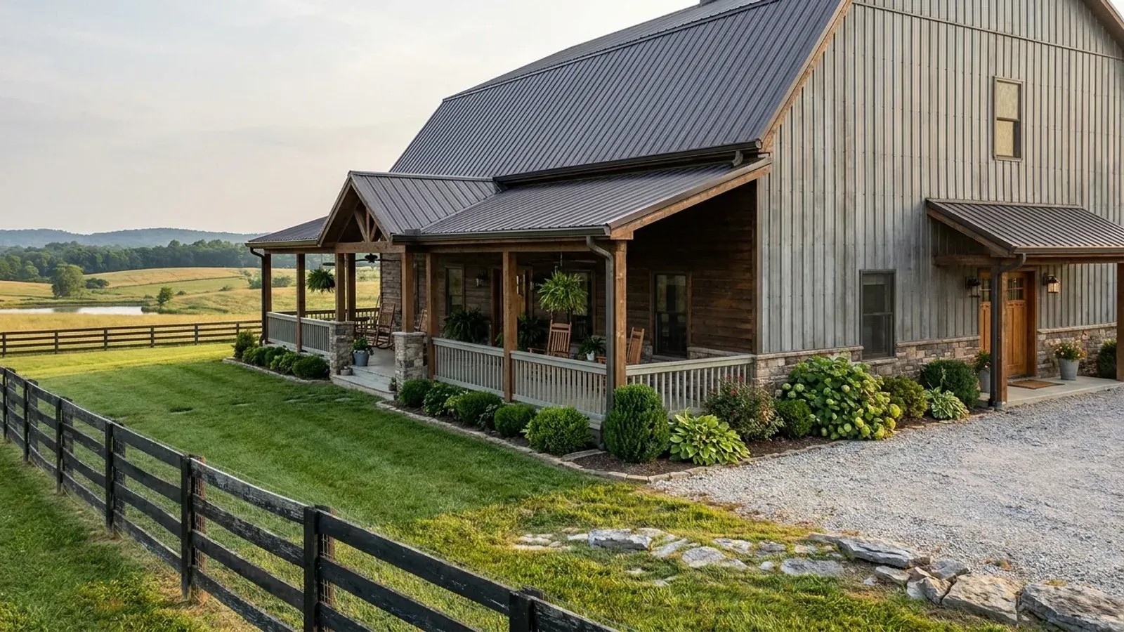 A barndominium exterior showing a deep wrap-around covered porch with posts and railing along two sides of the building.