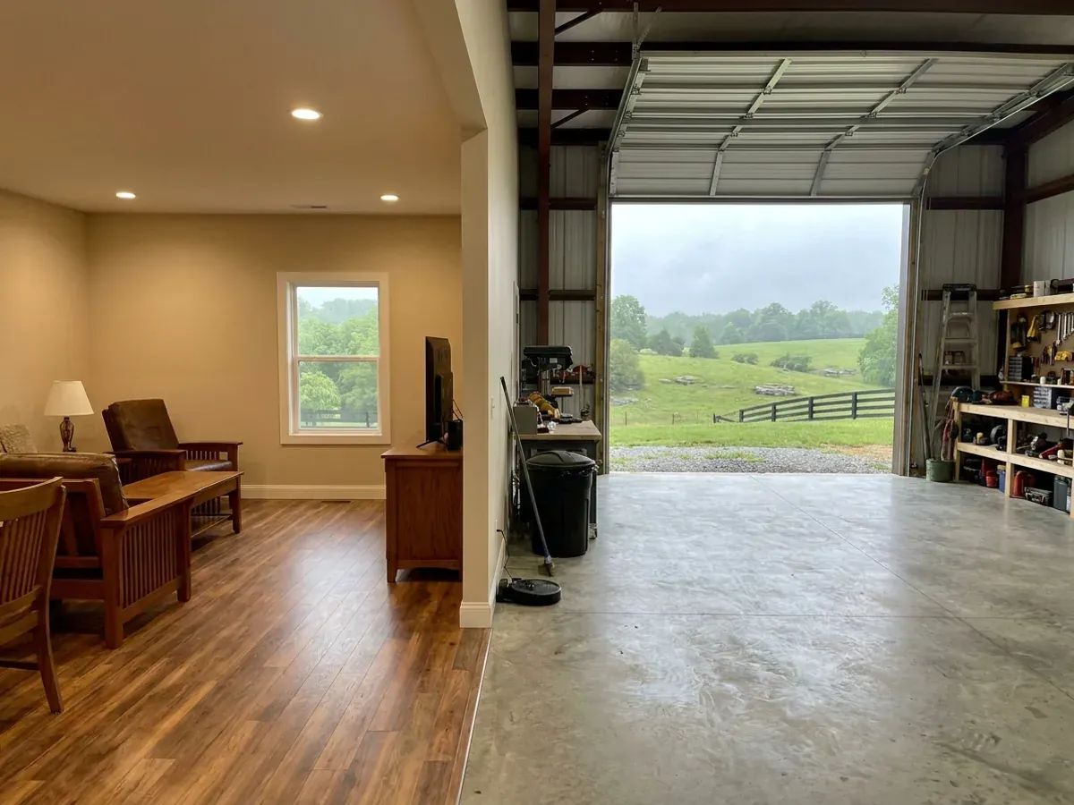 The interior of a shouse where a finished living area with warm flooring meets a shop bay with polished concrete and a tall roll-up door.