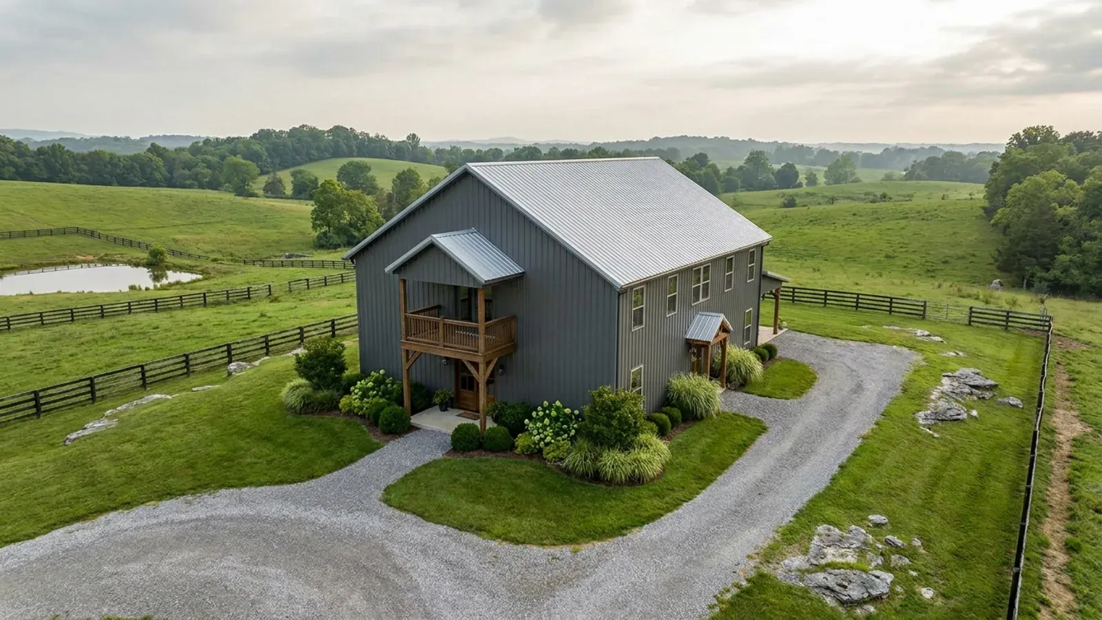A completed two-story barndominium with visible second-story windows and a small covered balcony above the entry porch.